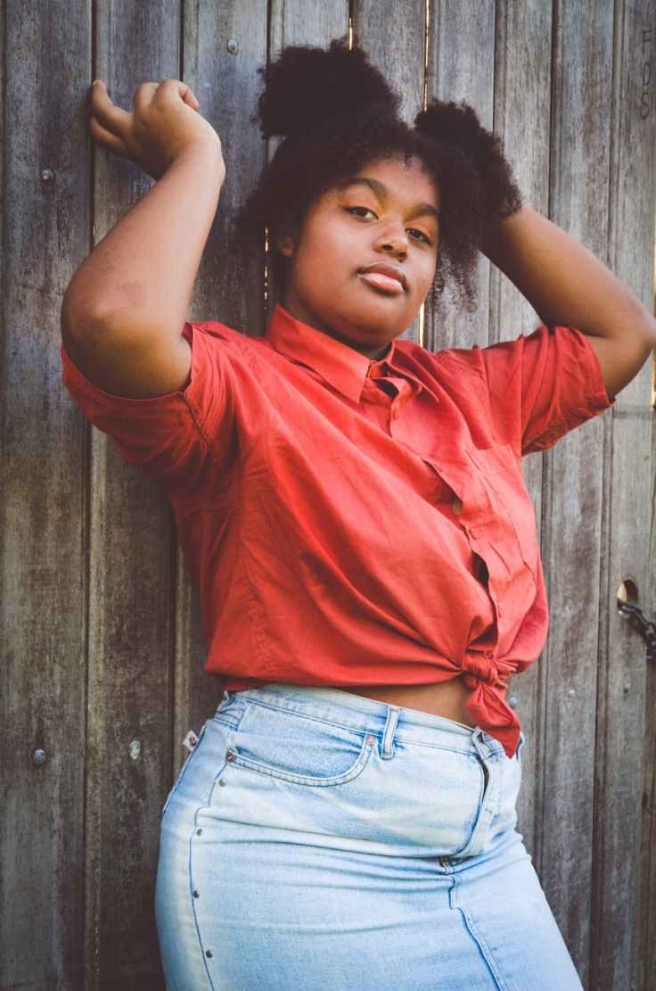 woman raising her arms while leaning on wooden fence